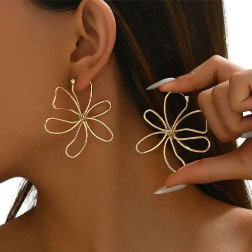 Gold-tone flower-shaped earrings with a swirling, open-petal design showcased on a person.