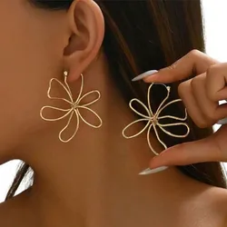 Gold-tone flower-shaped earrings with a swirling, open-petal design showcased on a person.