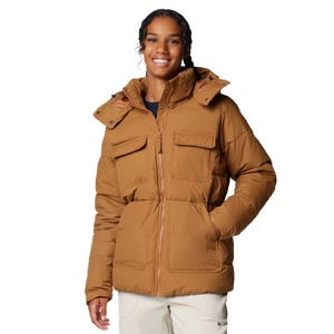A brown Columbia insulated jacket with a hood, featuring two chest pockets and two side pockets. The jacket is worn over a dark top and paired with light-colored pants.
