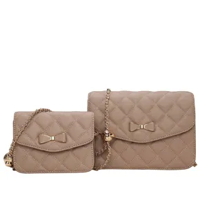 Two quilted handbags in a light brown color, featuring bow decorations and gold chain straps. One is larger and the other smaller, both with a similar design.