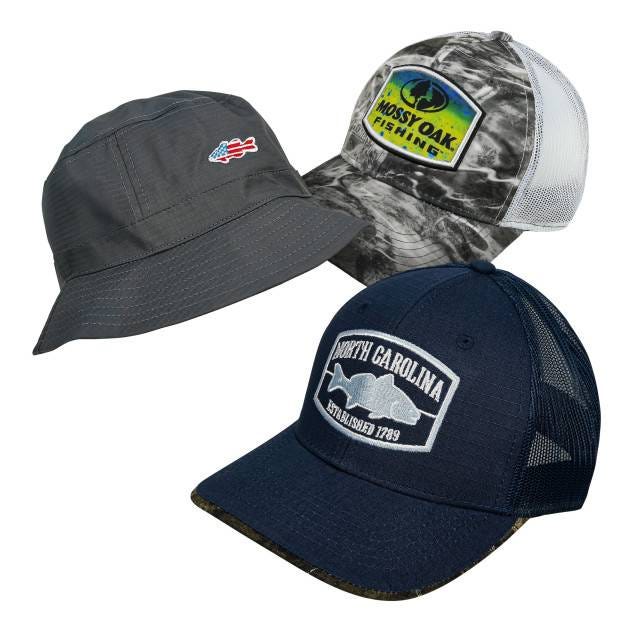 Three hats are shown: a gray bucket hat with a small flag patch, a camo mesh-back cap with a \“Mossy Oak Fishing\“ logo, and a navy mesh-back cap with a \“North Carolina Established 1789\“ patch.