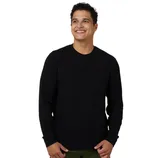 A smiling person wearing a black long-sleeve sweater and olive green pants stands against a gray background.