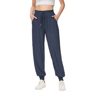 Navy blue high-waisted joggers with a drawstring waist, side pockets, and elastic cuffs at the ankles. The person is wearing white sneakers.