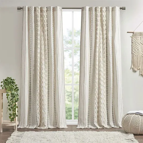 Beige and white patterned curtains hang from a rod in front of a window, with a small side table featuring a potted plant and a textured wall decoration nearby.