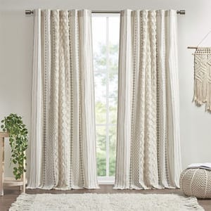 Beige and white patterned curtains hang from a rod in front of a window, with a small side table featuring a potted plant and a textured wall decoration nearby.