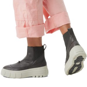 Person wearing black ankle-high boots with thick white soles, paired with rolled-up pink pants.