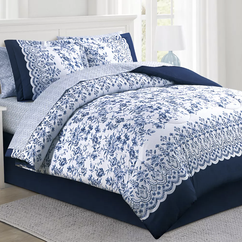 Blue and white floral-patterned bedding set with scalloped edges, including a comforter and matching pillow shams, on a bed with a white headboard.