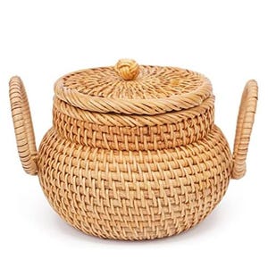 A woven rattan teapot-shaped basket with a lid and two handles, designed for decorative or storage purposes.