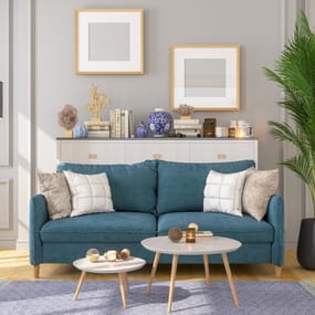 A teal sofa with cushions, accompanied by a white round coffee table, a tripod floor lamp, and a potted plant in a living room.
