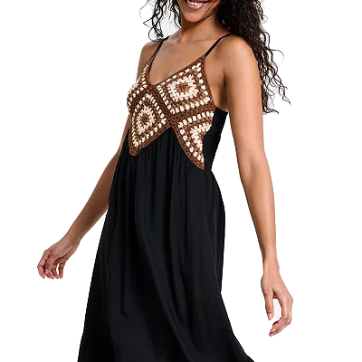 A woman is wearing a black dress with a crochet top featuring brown and white geometric patterns. The dress has thin straps and an empire waistline.