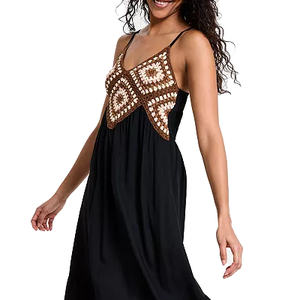 A woman is wearing a black dress with a crochet top featuring brown and white geometric patterns. The dress has thin straps and an empire waistline.