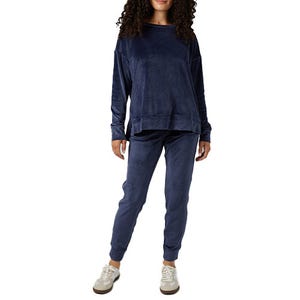 A person is wearing a dark blue velour tracksuit with a loose-fitting top and jogger-style pants, paired with white sneakers.