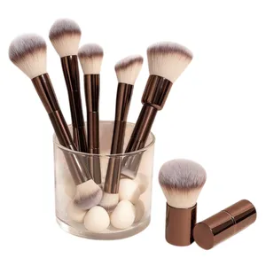 A collection of makeup brushes with light bristles and dark handles is displayed in a glass container filled with blending sponges.