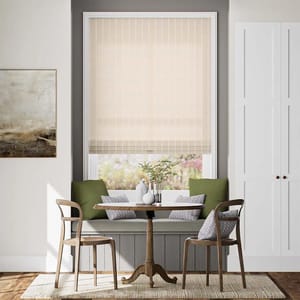 A cozy dining nook featuring a round wooden table, two chairs, a built-in bench with green and patterned cushions, a light-colored window shade, and a decorative wall painting.