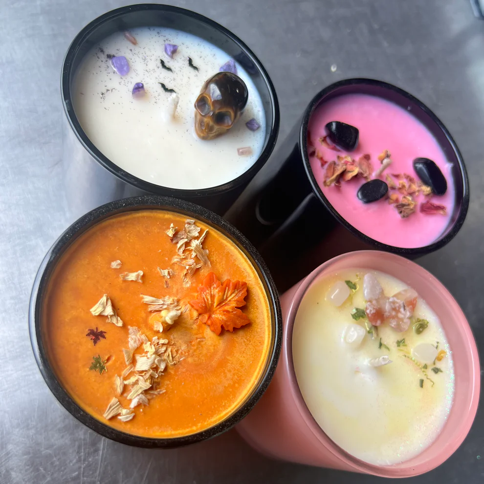 Four colorful candles in different cups, each featuring unique garnishes like a skull, leaves, and other decorative elements.