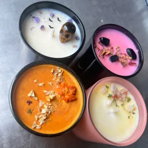 Four colorful candles in different cups, each featuring unique garnishes like a skull, leaves, and other decorative elements.