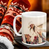 A white mug featuring a festive holiday photo is set against warm, cozy socks with a red and white snowflake pattern.