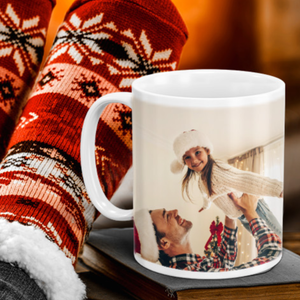 A white mug featuring a festive holiday photo is set against warm, cozy socks with a red and white snowflake pattern.