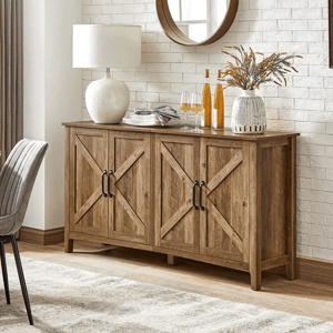 A rustic-style buffet cabinet with a wood finish and cross-patterned doors, featuring four handles. It is adorned with decorative items like a table lamp, plates, glasses, a vase, and bottles, set against a white brick wall.