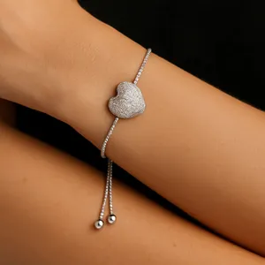 A silver adjustable bracelet with a textured heart pendant, featuring a thin chain and two small metallic beads as part of the closure.