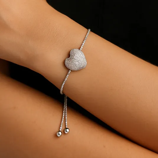 A silver adjustable bracelet with a textured heart pendant, featuring a thin chain and two small metallic beads as part of the closure.