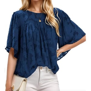 A navy blue babydoll blouse with a textured pattern, featuring flowy sleeves and pleated detailing on the chest. Paired with white high-waisted pants, a gold necklace, and a light-colored clutch.