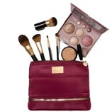 A burgundy makeup bag with a gold zipper displaying various brushes, a face palette with different powders, and a compact powder.
