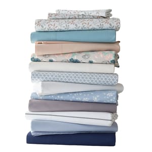 A stack of folded bed sheets in various colors and patterns, including floral and solid designs.