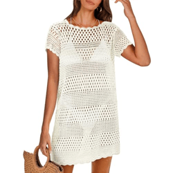 A woman wearing a short-sleeve, cream-colored crochet dress stands holding a woven handbag.