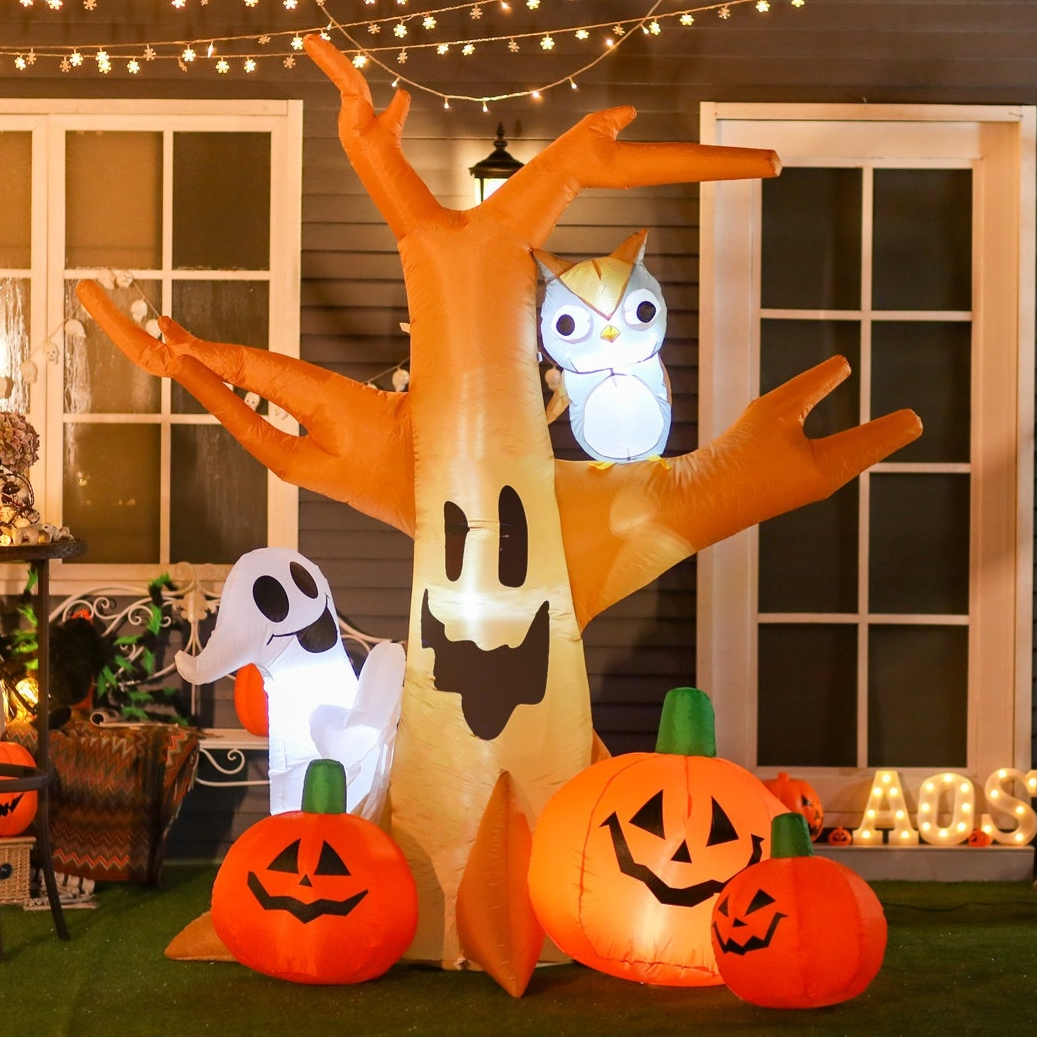 Inflatable Halloween decorations featuring a smiling ghost, pumpkins with faces, an owl, and a spooky tree, set against a house with fairy lights.