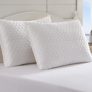 Two white Tommy Bahama pillows with a hexagonal quilted pattern are placed on a bed. They feature a clean, crisp design, suitable for a modern bedroom setting.