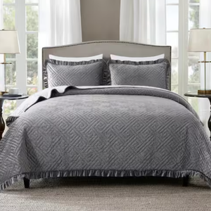 A 3-piece King Velvet Quilt Set in gray features a geometric pattern quilt and two matching pillow shams. The quilt has a ruffled edge, and the set creates a sophisticated look in the bedroom.