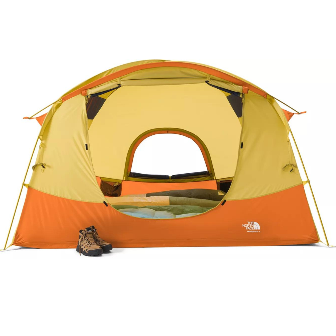 A yellow and orange The North Face Sequoia tent with an open door, revealing a sleeping bag inside; a pair of hiking boots sits outside.