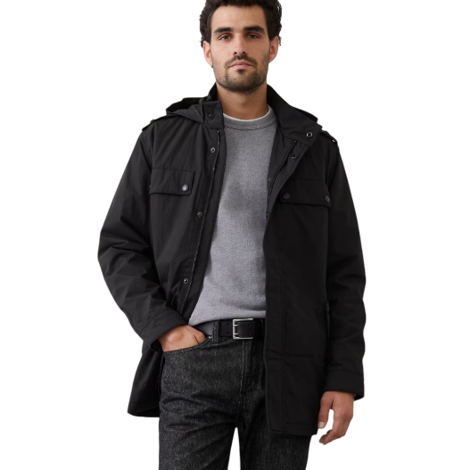 A man is wearing a black hooded jacket over a gray sweater, paired with dark jeans and a black belt.