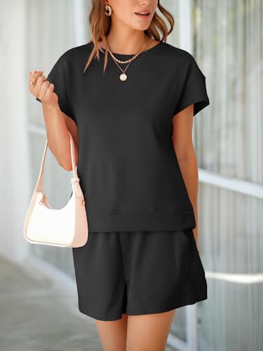 A woman wears a short-sleeve, textured black top and matching shorts, accessorized with a white shoulder bag and layered necklaces.