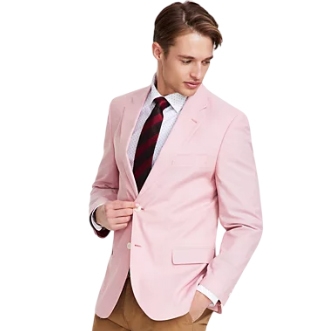 A man is wearing a light pink Nautica Chambray Sport Coat, featuring a two-button front, notch lapels, and a chest pocket. He's paired it with a patterned dress shirt, a red and black tie, and brown pants.