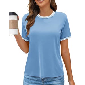 A woman is wearing a light blue short-sleeve top with white trim at the collar and sleeves. She holds a coffee cup and pairs the top with blue jeans.