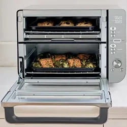 A countertop oven with two cooking racks contains baked goods on the top and a dish with salmon and broccoli on the lower rack.