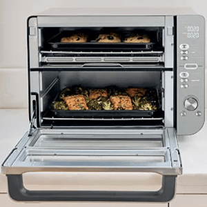 A countertop oven with two cooking racks contains baked goods on the top and a dish with salmon and broccoli on the lower rack.