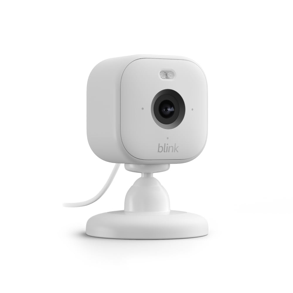 A compact, white Blink Mini 2 Camera with a rectangular shape and rounded edges, featuring a central lens, a small infrared sensor on top, and mounted on a short stand with a connecting cable.