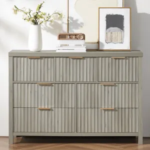 A gray dresser with ribbed drawer fronts is topped with decorative items: a white vase with flowers, a vintage-style radio, and framed artwork.