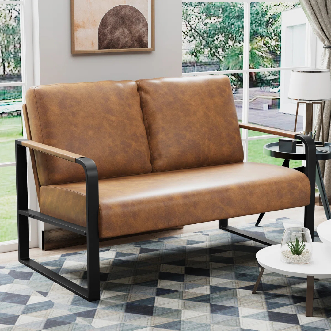 A modern brown leather loveseat with black metal frame and wooden armrests is placed in a stylish living room, featuring a geometric patterned rug and nearby side tables.