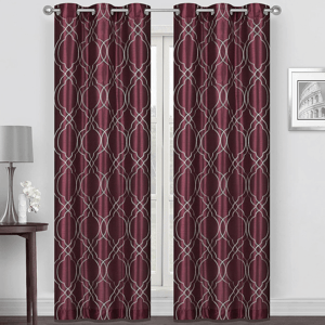 Burgundy curtain panels with a geometric silver pattern, hanging on a rod. They complement a minimalist room featuring a small table, a lamp, and a decorative flower vase.