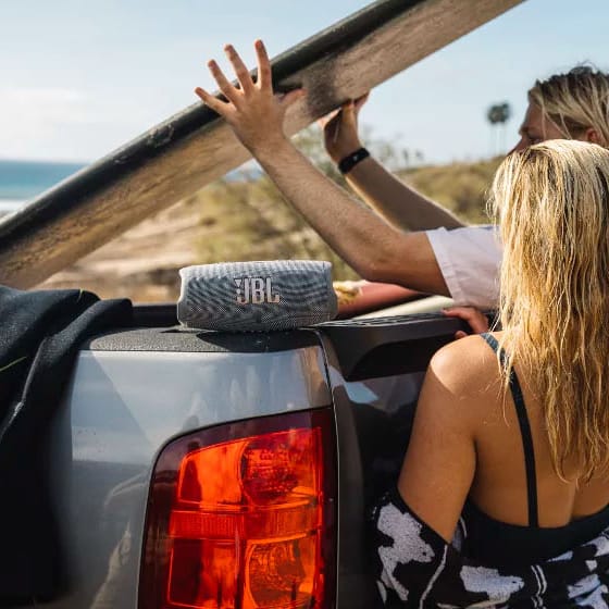 A JBL portable speaker on a car with two people prepping for a surf session.