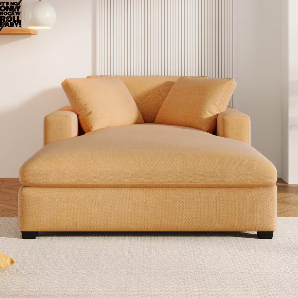 A large, mustard-colored chaise lounge with two matching pillows is placed in a bright living room with a white carpet and decorative wall elements.