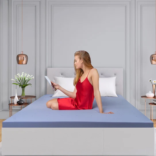A woman in a red dress is sitting on a bed with a blue sheet while reading a tablet.