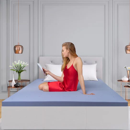 A woman in a red dress is sitting on a bed with a blue sheet while reading a tablet.