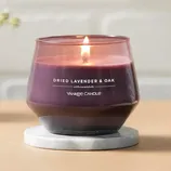 A lit Yankee Candle labeled \“Dried Lavender & Oak,\“ featuring a purple color, is placed on a marble coaster.