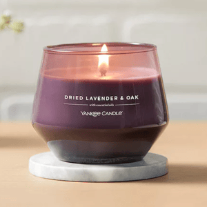 A lit Yankee Candle labeled \“Dried Lavender & Oak,\“ featuring a purple color, is placed on a marble coaster.