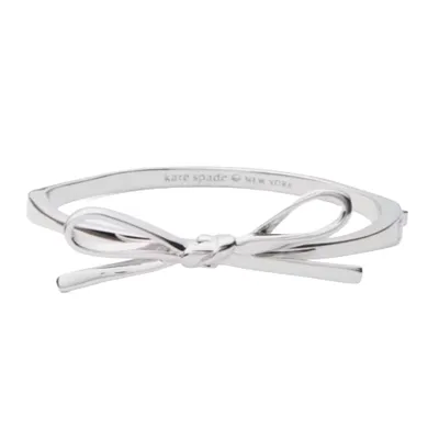 A silver bow bangle with a sleek, minimalist design, labeled \“kate spade NEW YORK\“ on the inside.